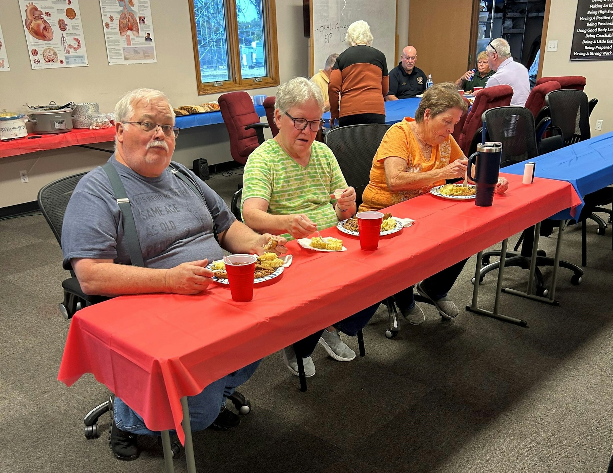 Three people eating at a table with a red tablecloth in a room with posters on the wall.
