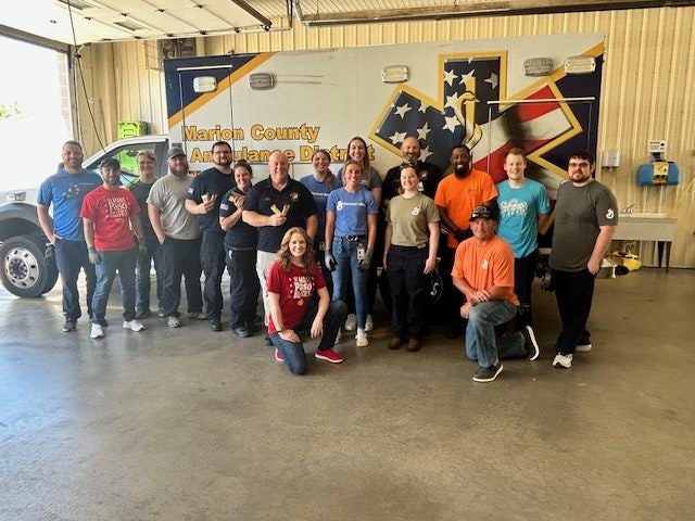 A group of people posing in front of an ambulance with "Marion County" written on it, likely a team of emergency responders or medical staff.