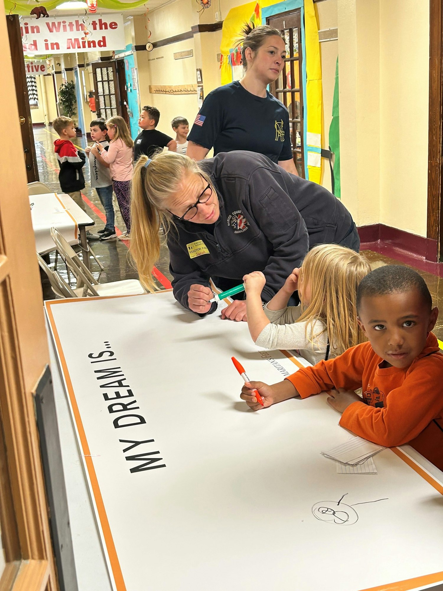 Adults and children in a school hallway writing on a banner that says "My Dream Is..."