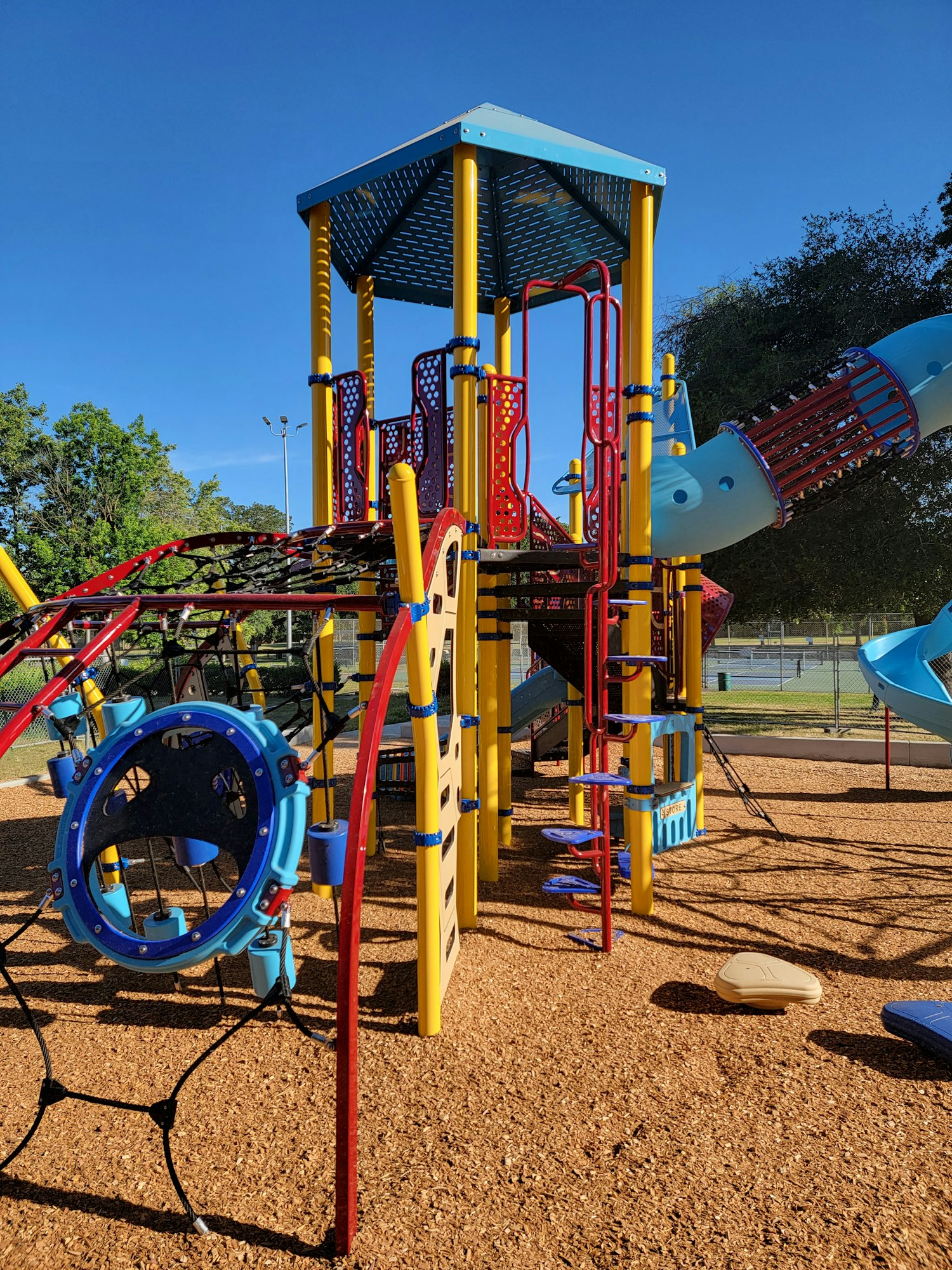 Colorful playground equipment with slides and climbing structures on wood chips, sunny day.
