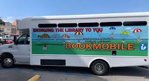 A white "Bookmobile" van with colorful graphics and the text "Bringing the Library to You!" on its side.