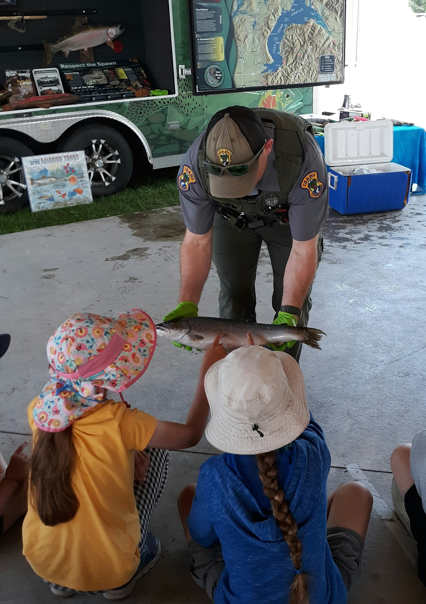A uniformed officer showing a fish to children with educational materials in the background.