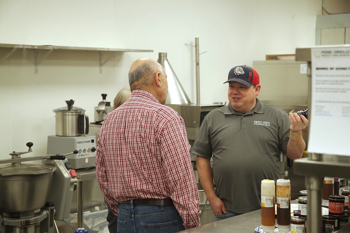 Two people talking in a kitchen with various cooking equipment and sauces.