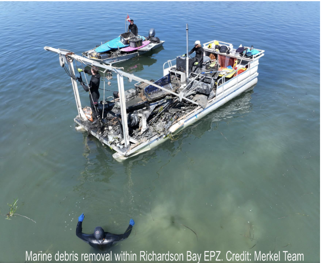 Divers removing marine debris from a water body, assisted by a small boat loaded with trash.