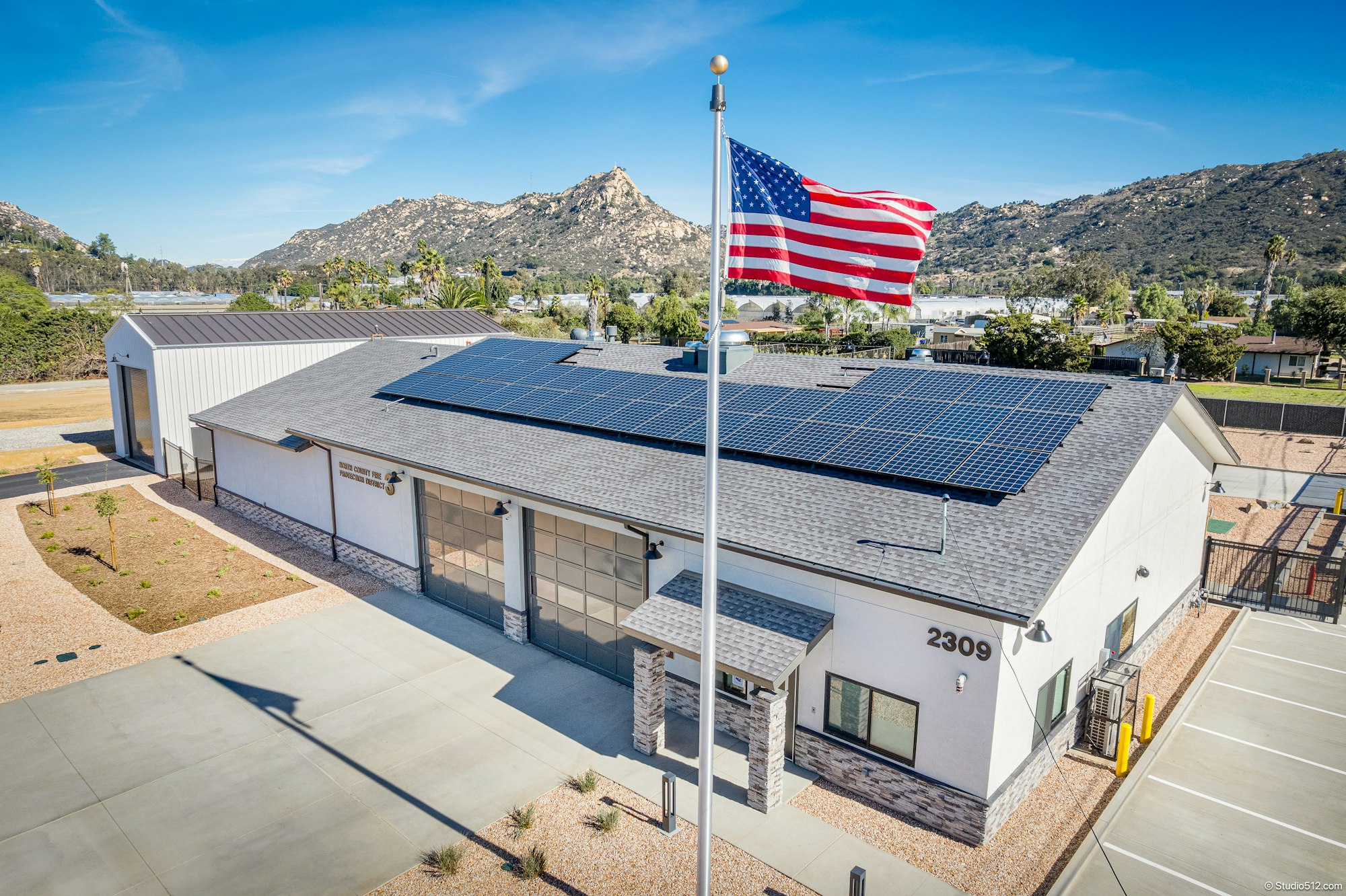 A modern, solar-paneled building with a US flag, set against a mountainous backdrop, likely a fire station or community center.