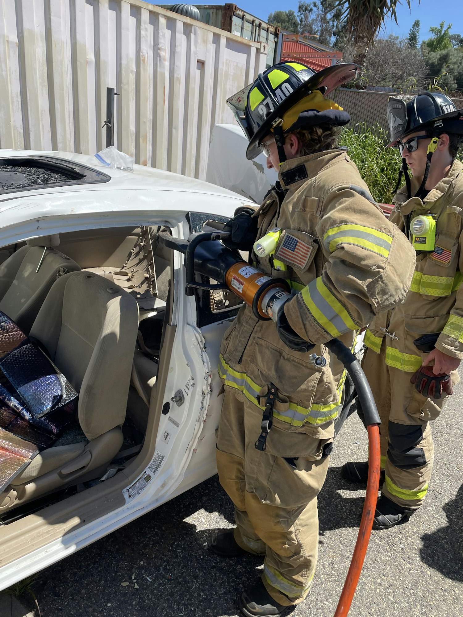Firefighters with equipment near a car, possibly during a rescue or training exercise. Image is rotated.
