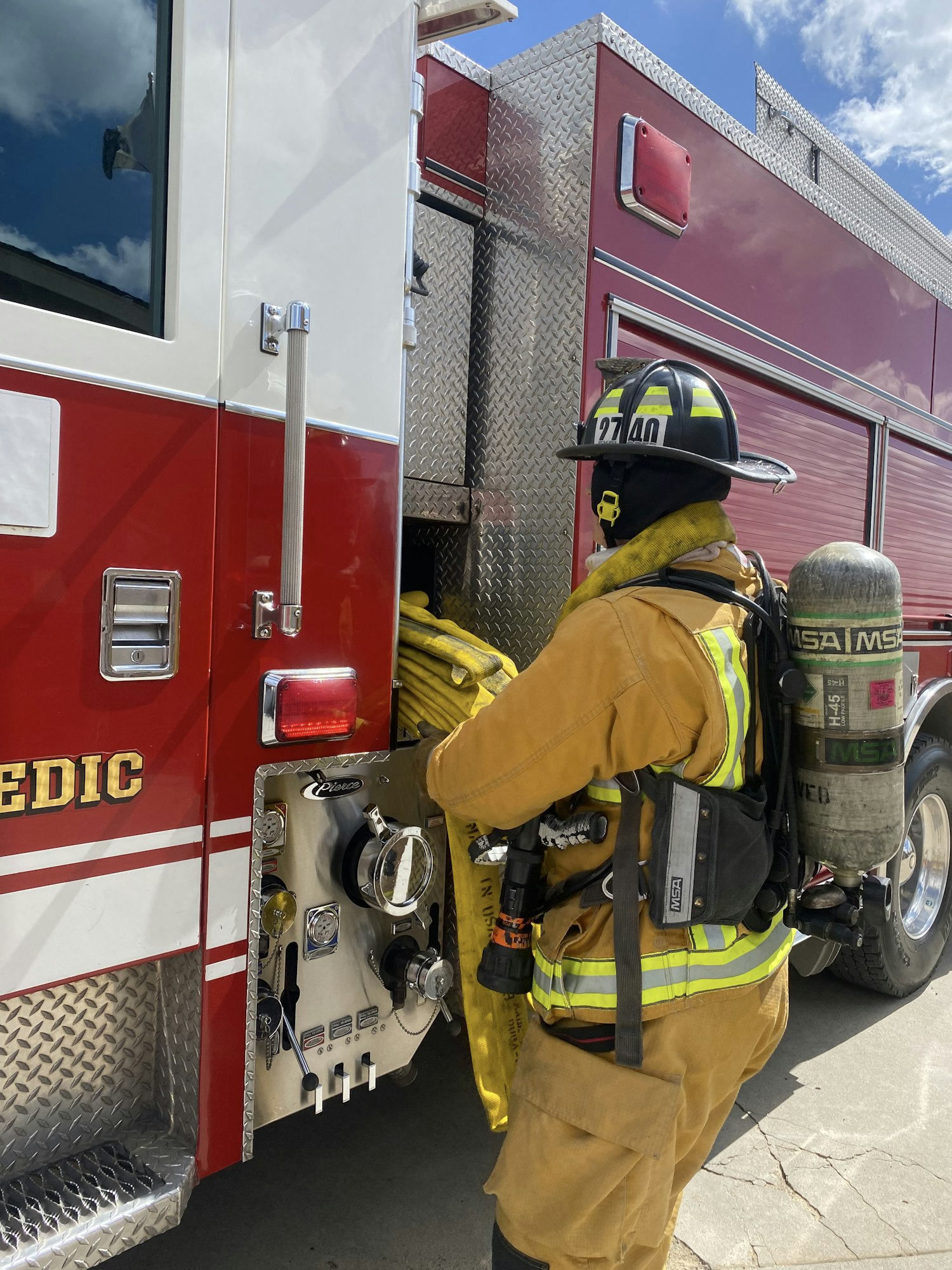 A firefighter in full gear standing beside a red fire truck.