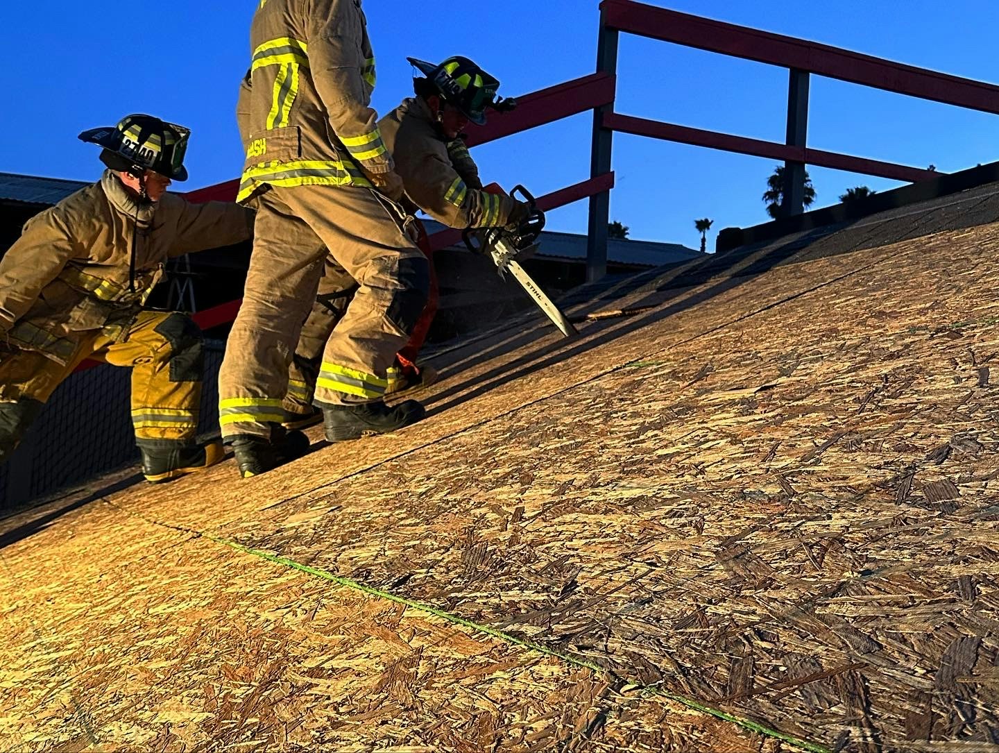 Firefighters on a roof with tools at sunset.