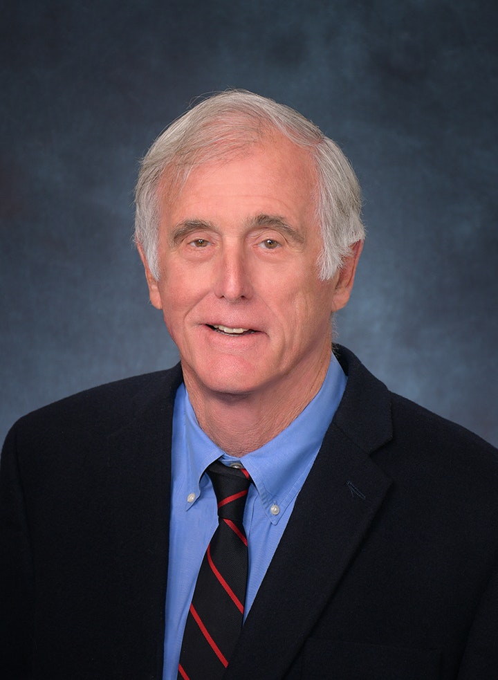 A person in a suit and tie against a gray background.