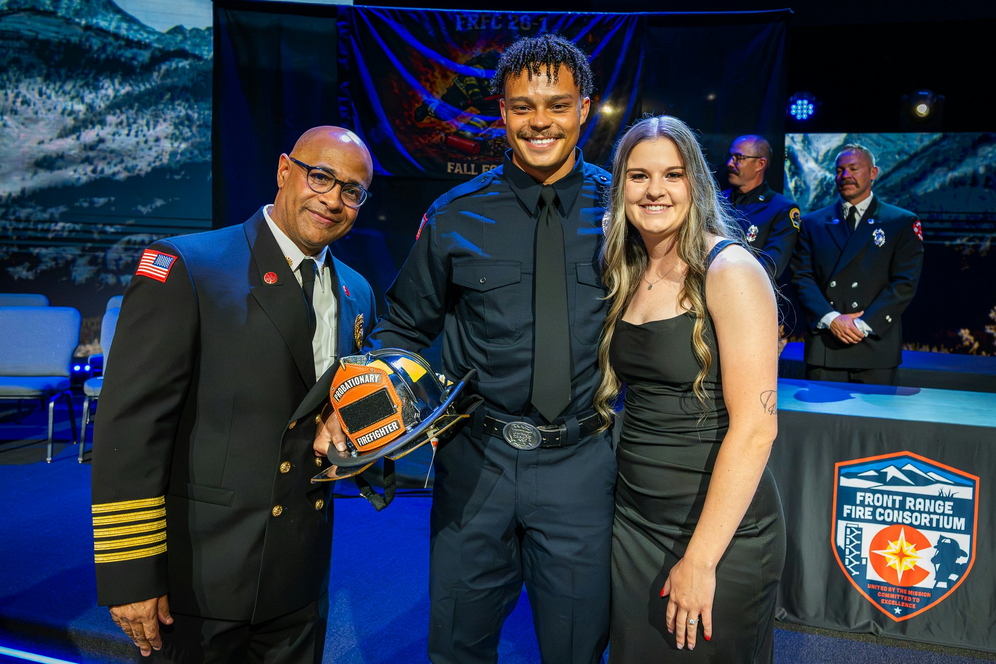 A ceremony featuring a firefighter in uniform receiving an award, posing with a chief and a woman, celebrating an achievement.