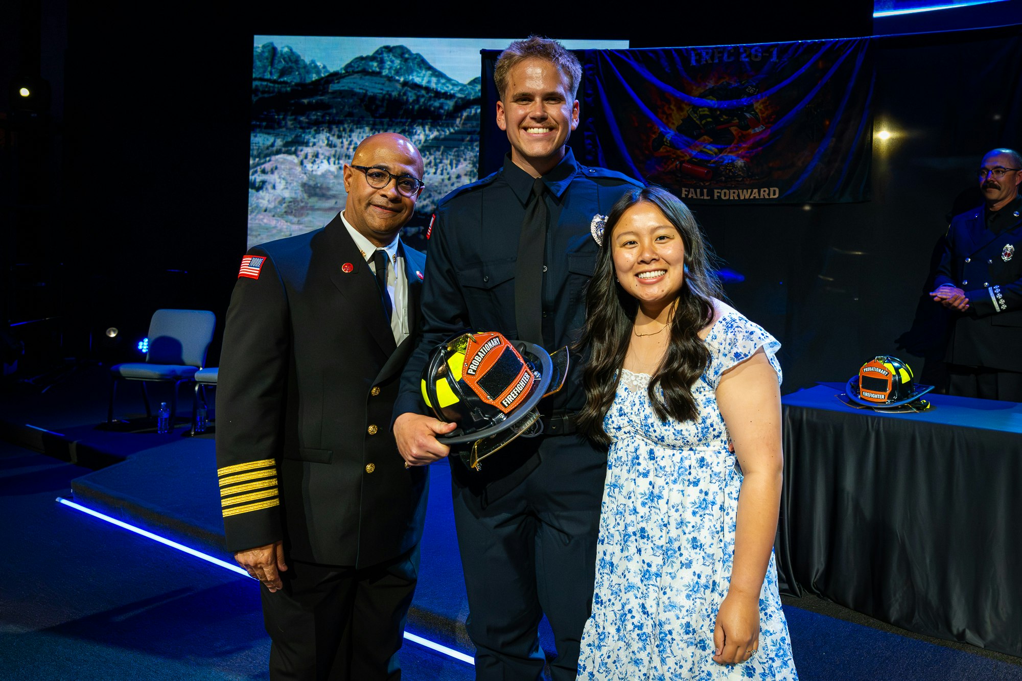 A group poses for a photo at a ceremony, celebrating a firefighter's achievement, holding a helmet and smiling.