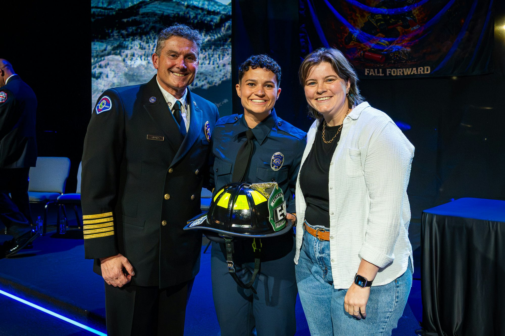 A ceremony featuring a firefighter and supporters, highlighting achievements with a helmet and uniforms displayed.
