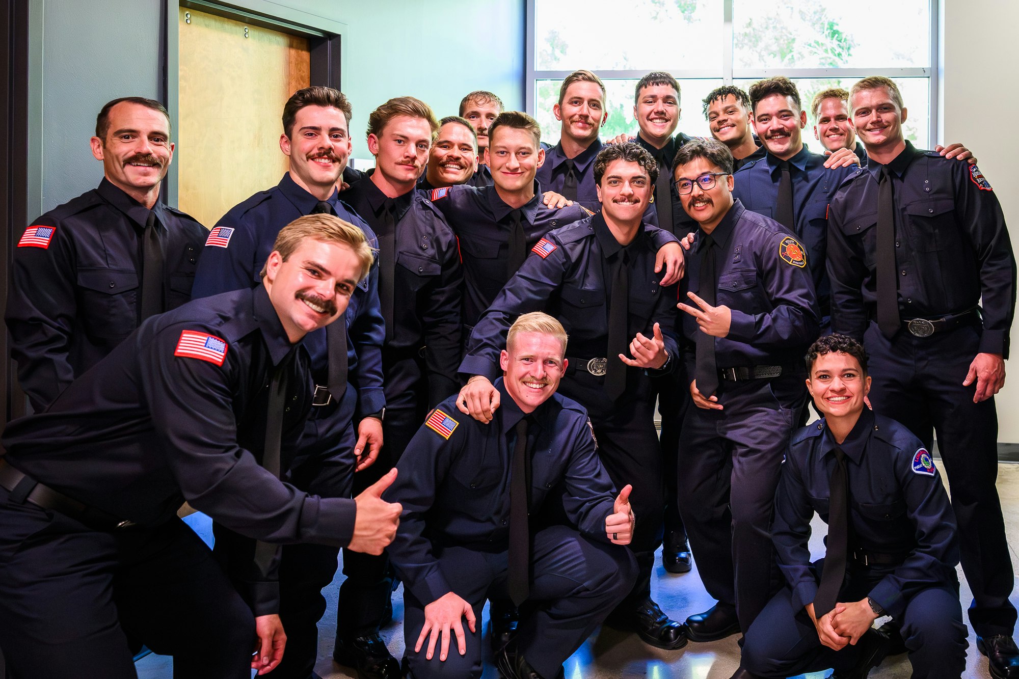 A group of smiling individuals in uniforms, some with mustaches, posing together in a celebratory setting.