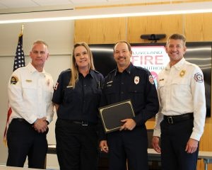 Four firefighters posing for a photo; one is holding a certificate.