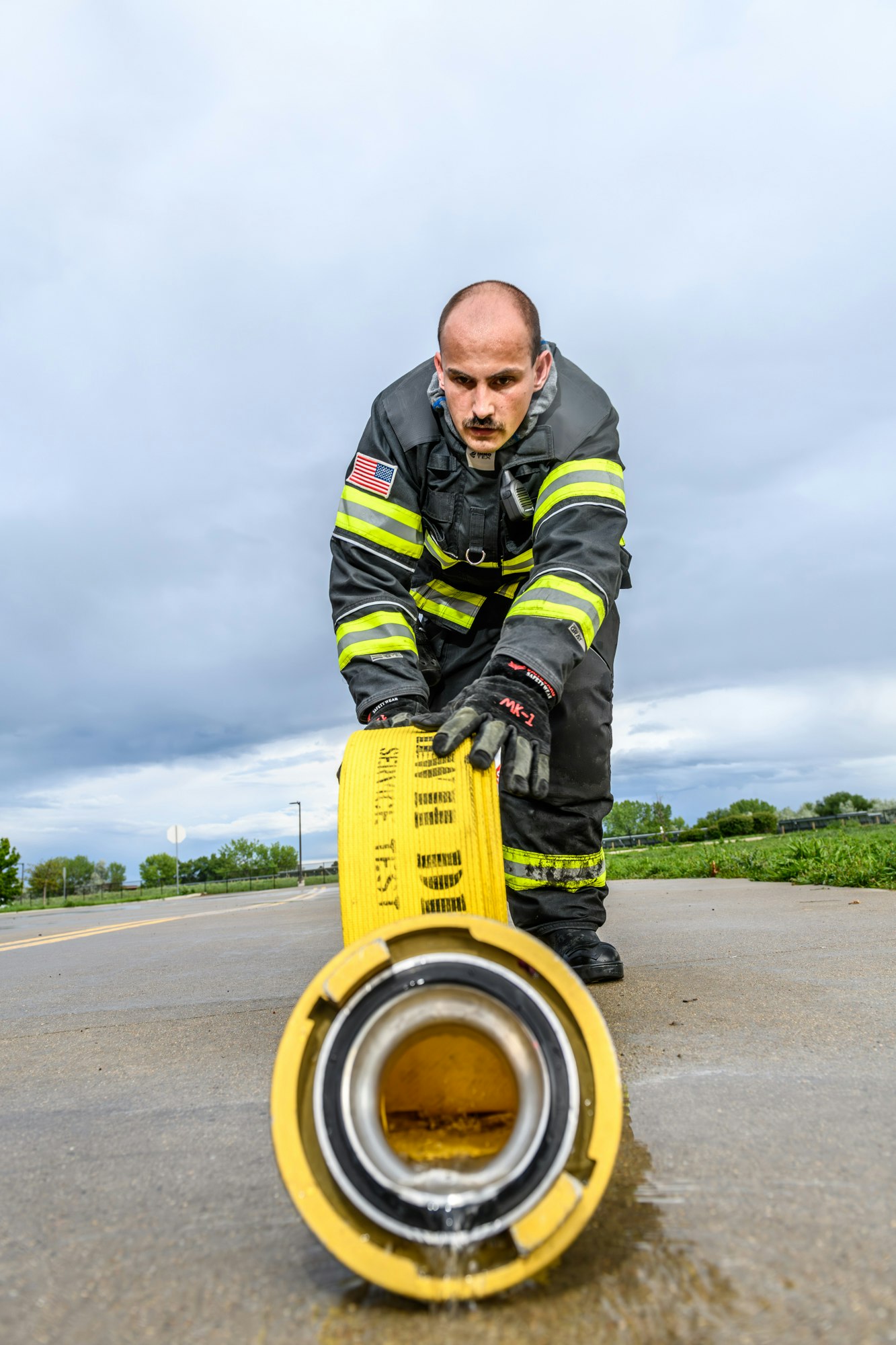 A firefighter rolling out a yellow fire hose on a wet pavement.