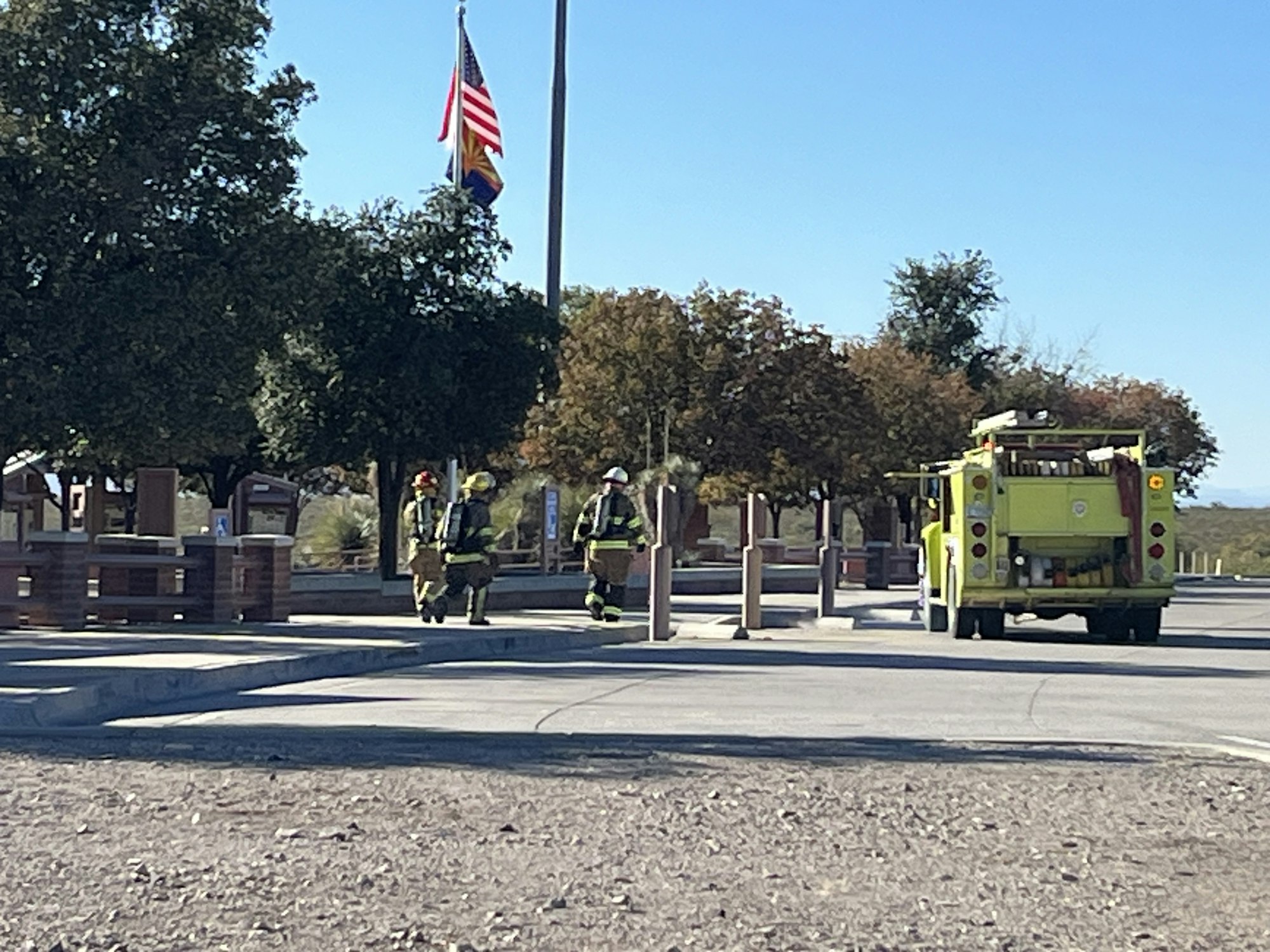 Firefighters walking near a fire truck with two flags in the background.