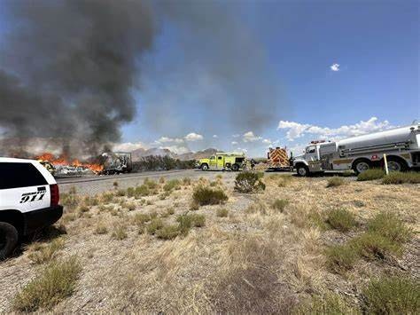 Emergency vehicles respond to a fire near a road, with smoke and flames visible in the background.