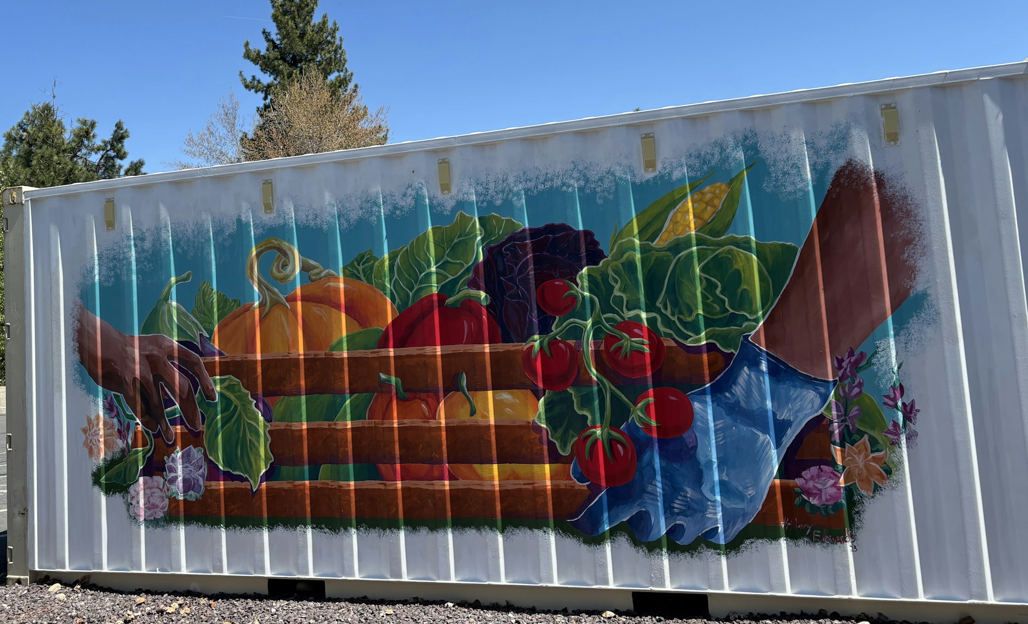 A colorful mural of vegetables and two hands on a white surface, with trees in the background.