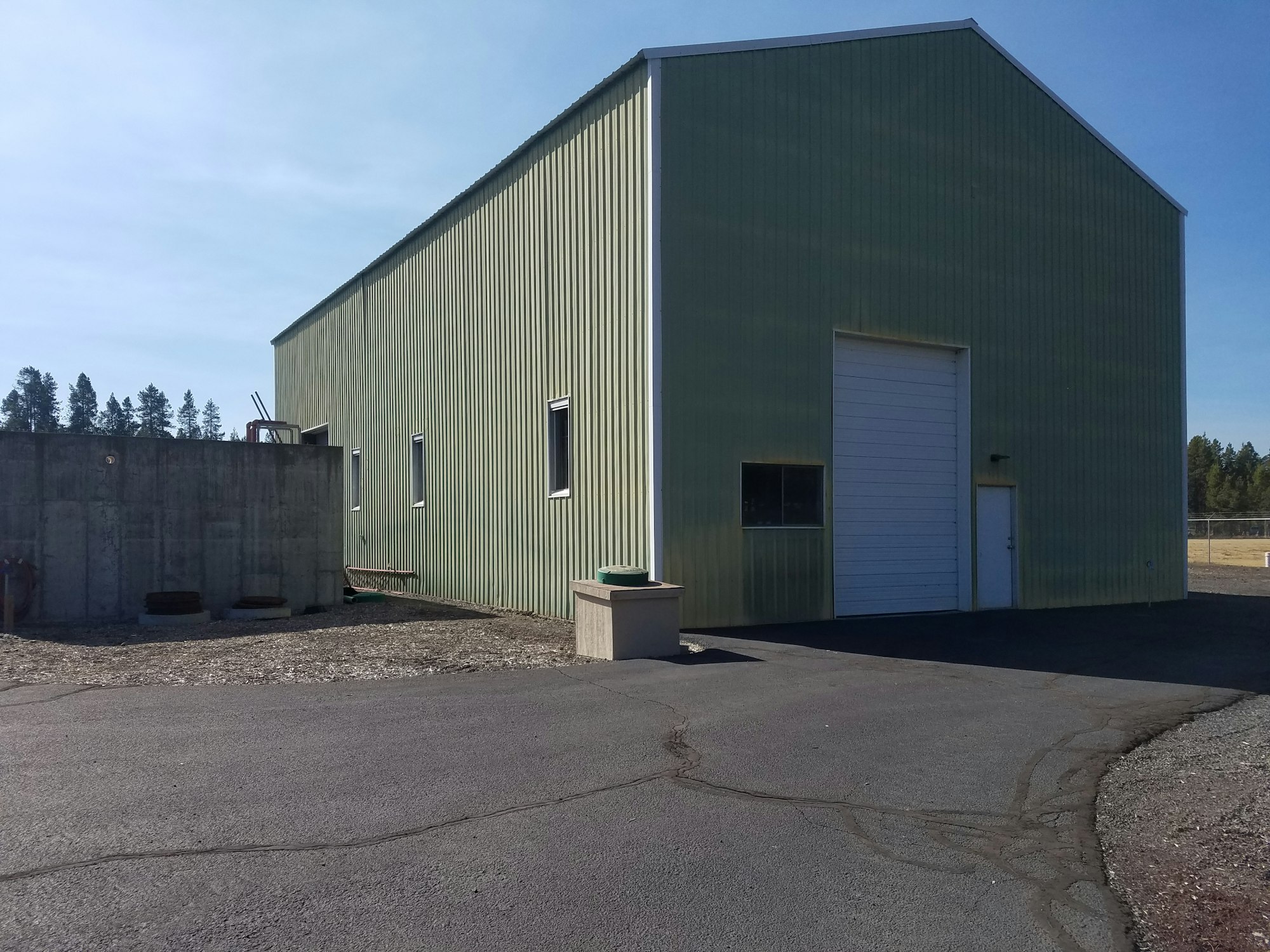 Green industrial building with a white door, concrete wall, and clear sky.