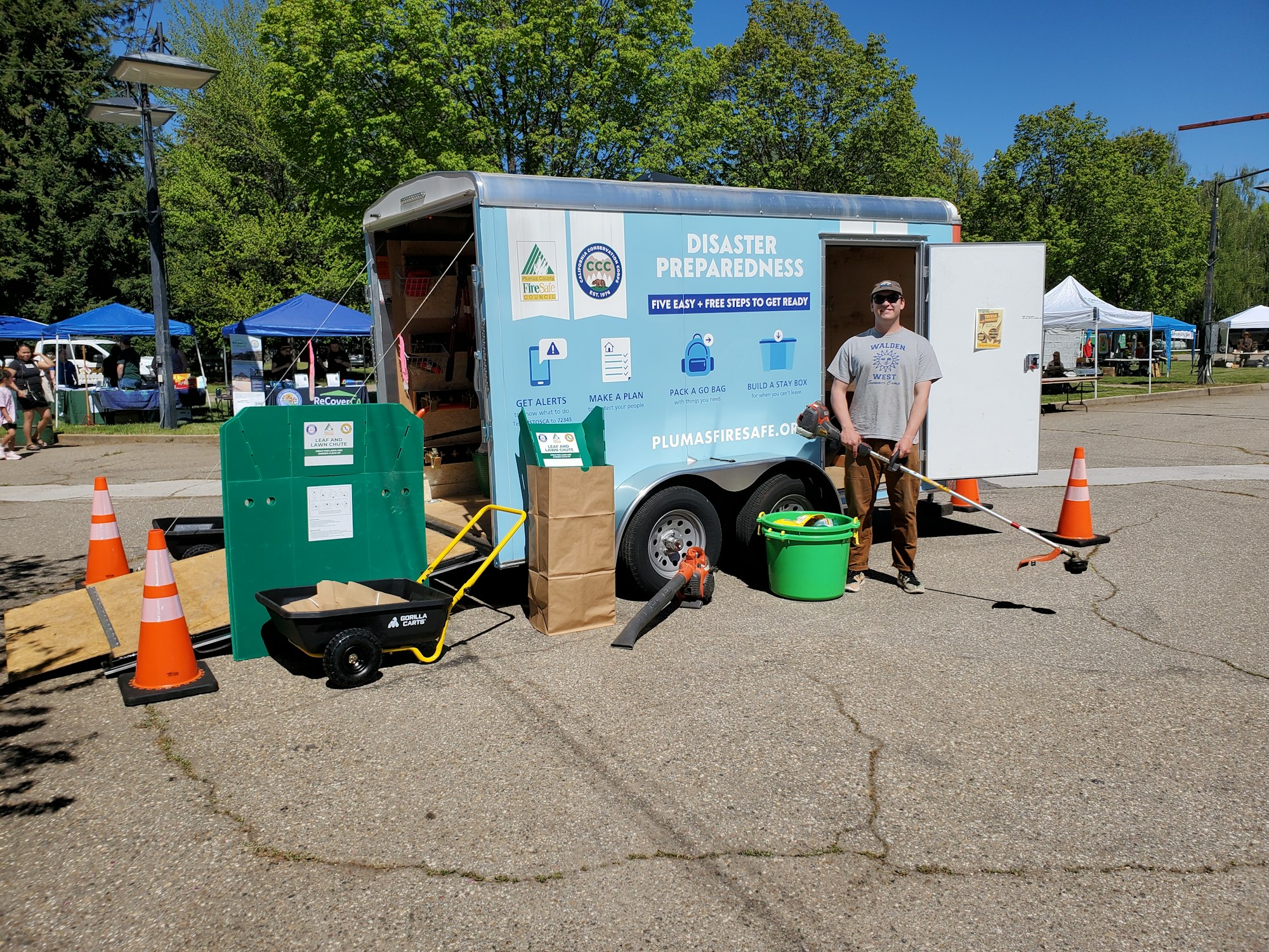 A disaster preparedness trailer with a smiling person holding a tool, surrounded by supplies and informational signs.