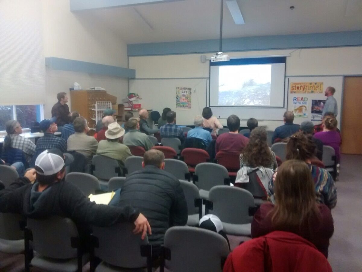 A group of people seated in a room watching a presentation projected on a screen.