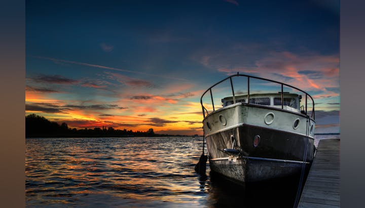 A boat docked at sunset, with vibrant colors reflecting on the water and a serene atmosphere.