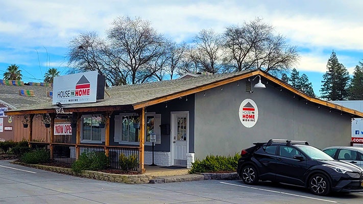 A small building labeled "House to Home," offering supplies. A "Now Open" sign is visible. A black car is parked in front.