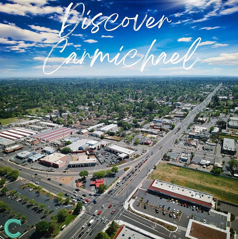 Aerial view of Carmichael with roads, buildings, and greenery under a blue sky. Text reads "Discover Carmichael."