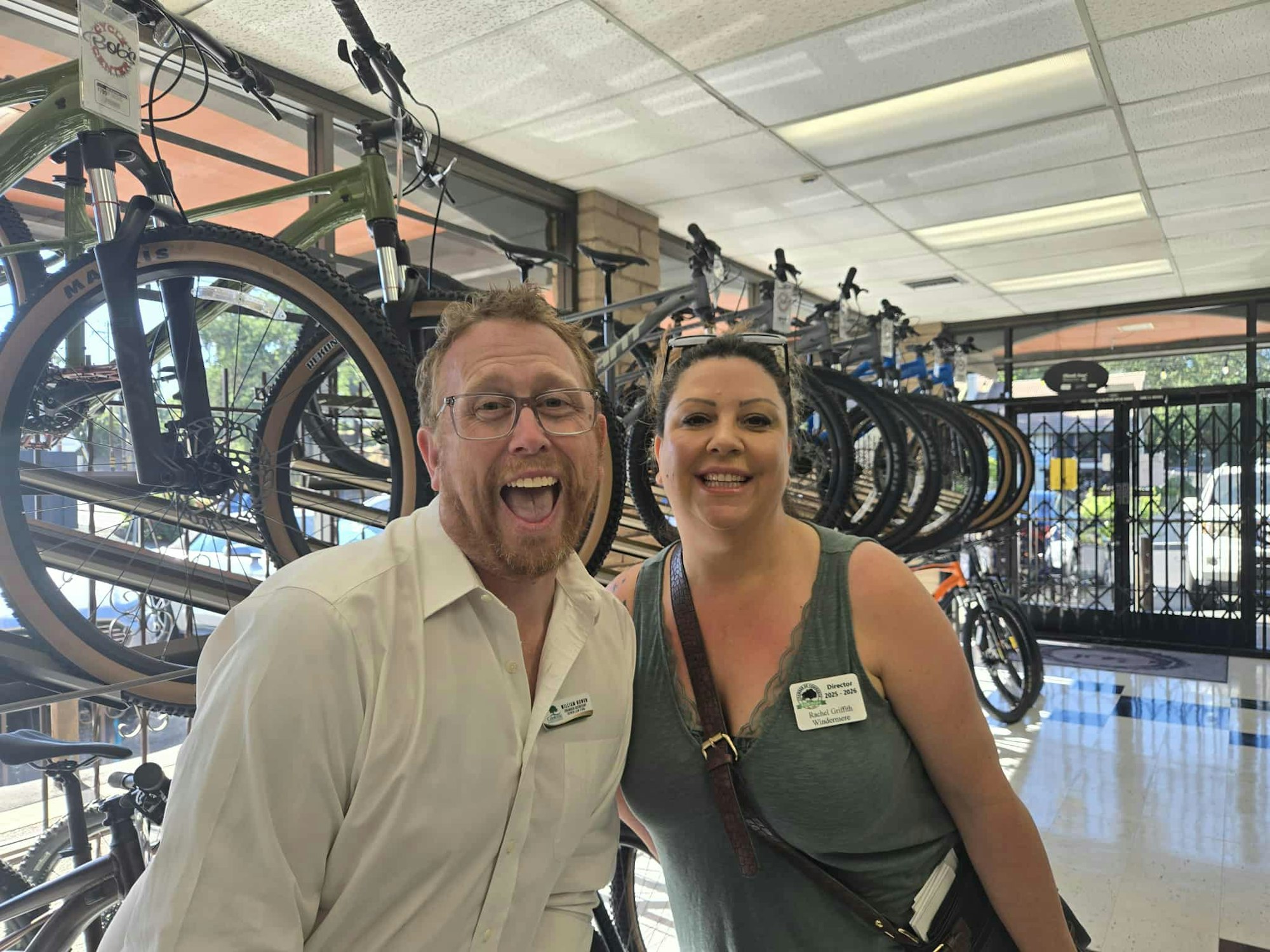 Two people smiling in a bike shop with bicycles on display behind them.