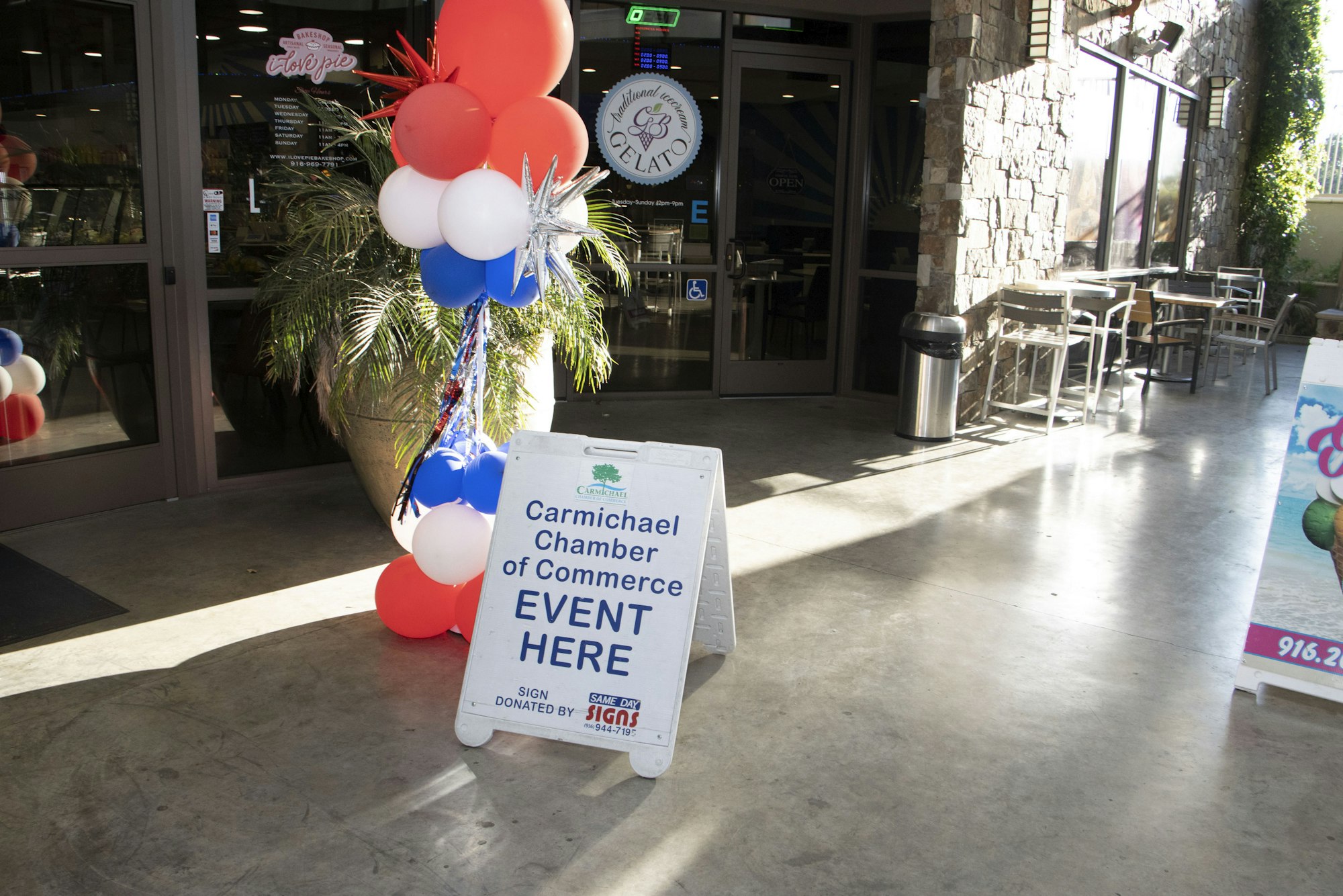 Storefront with balloons and a sign for a Carmichael Chamber of Commerce event.