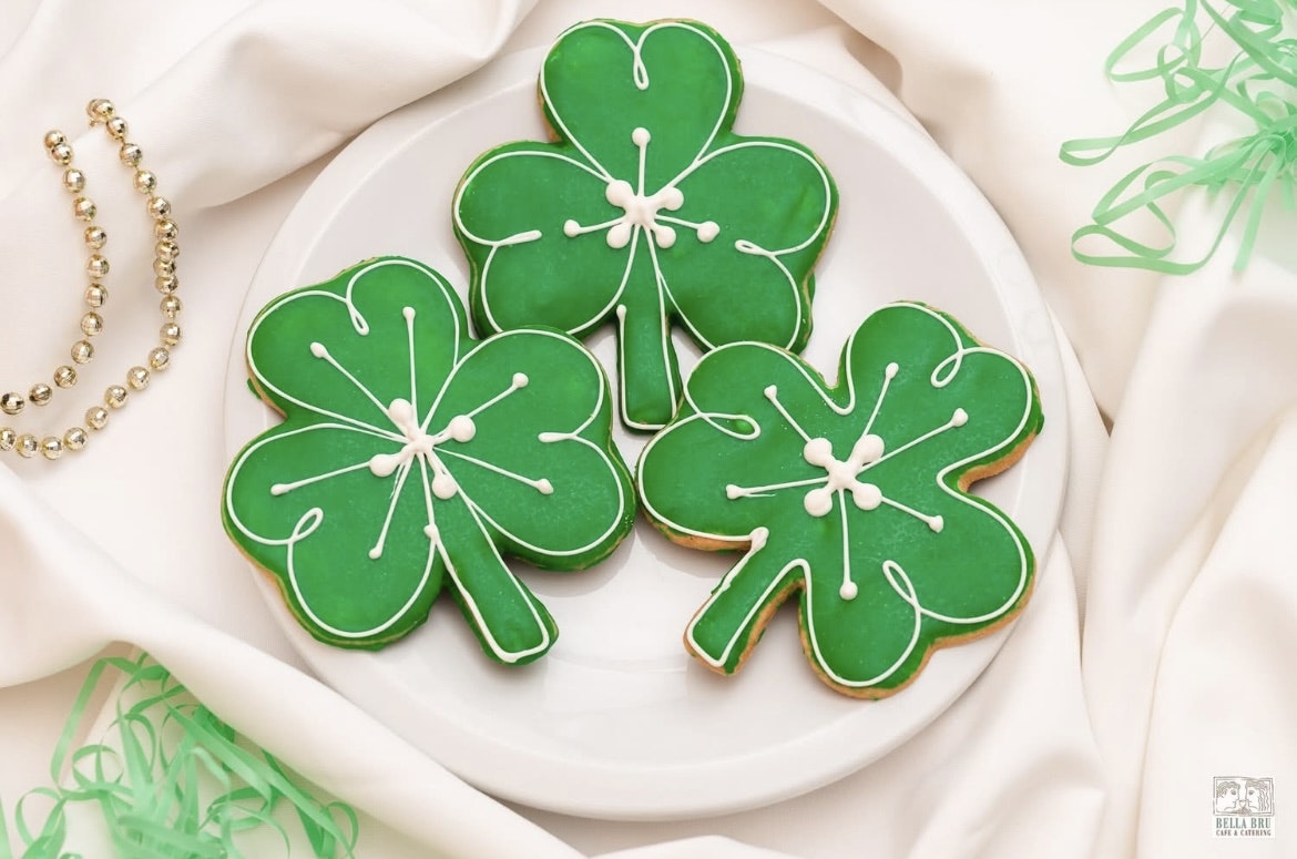 Plate with three shamrock-shaped green cookies and decorative beads on a white fabric background.