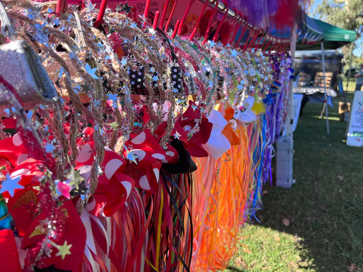 A colorful display of decorative hair accessories featuring ribbons, bows, and sparkles, showcased at an outdoor event.