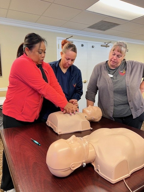 Three people practicing CPR on mannequins at a table.