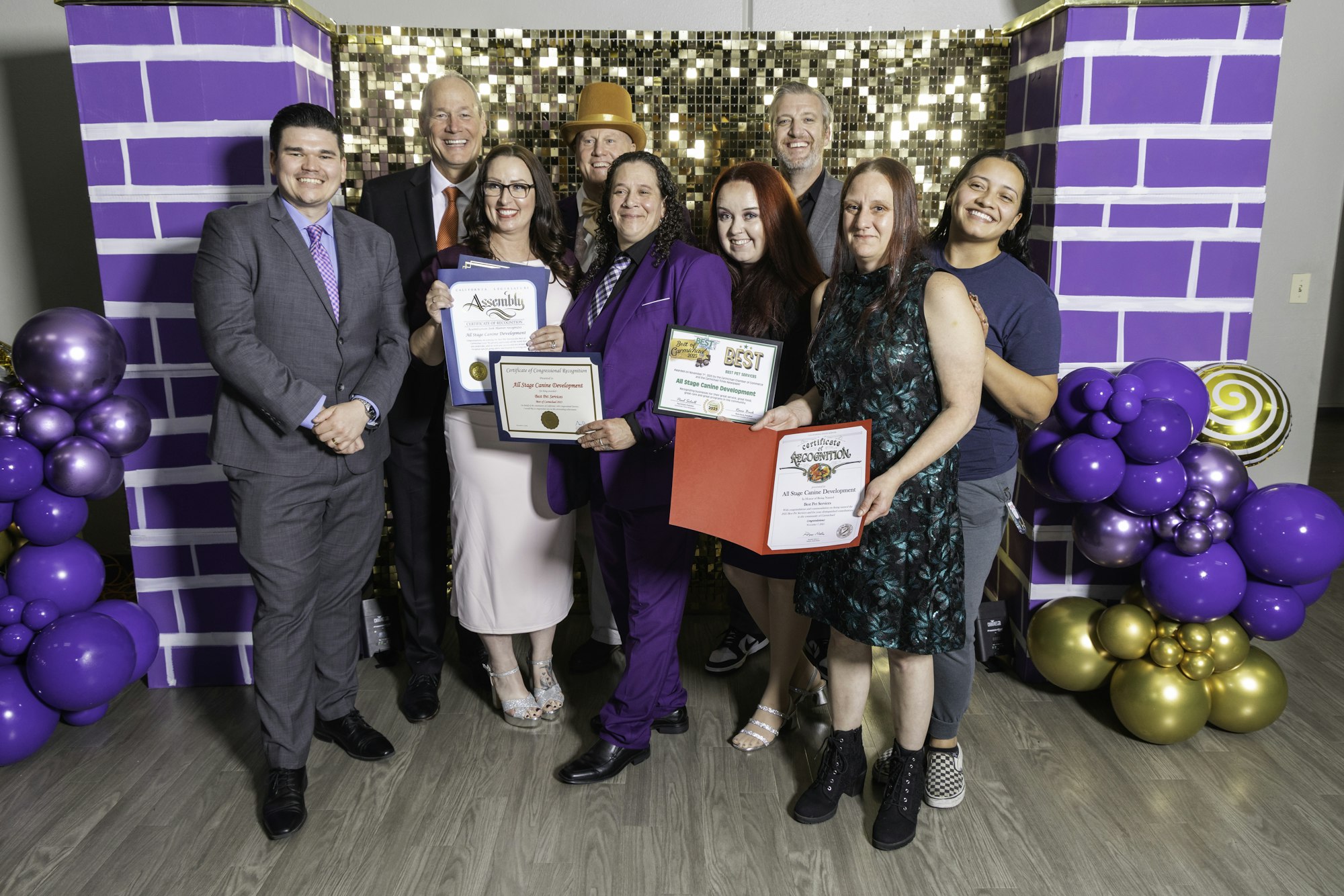 A group of people posing with certificates against a festive backdrop of purple and gold decorations.
