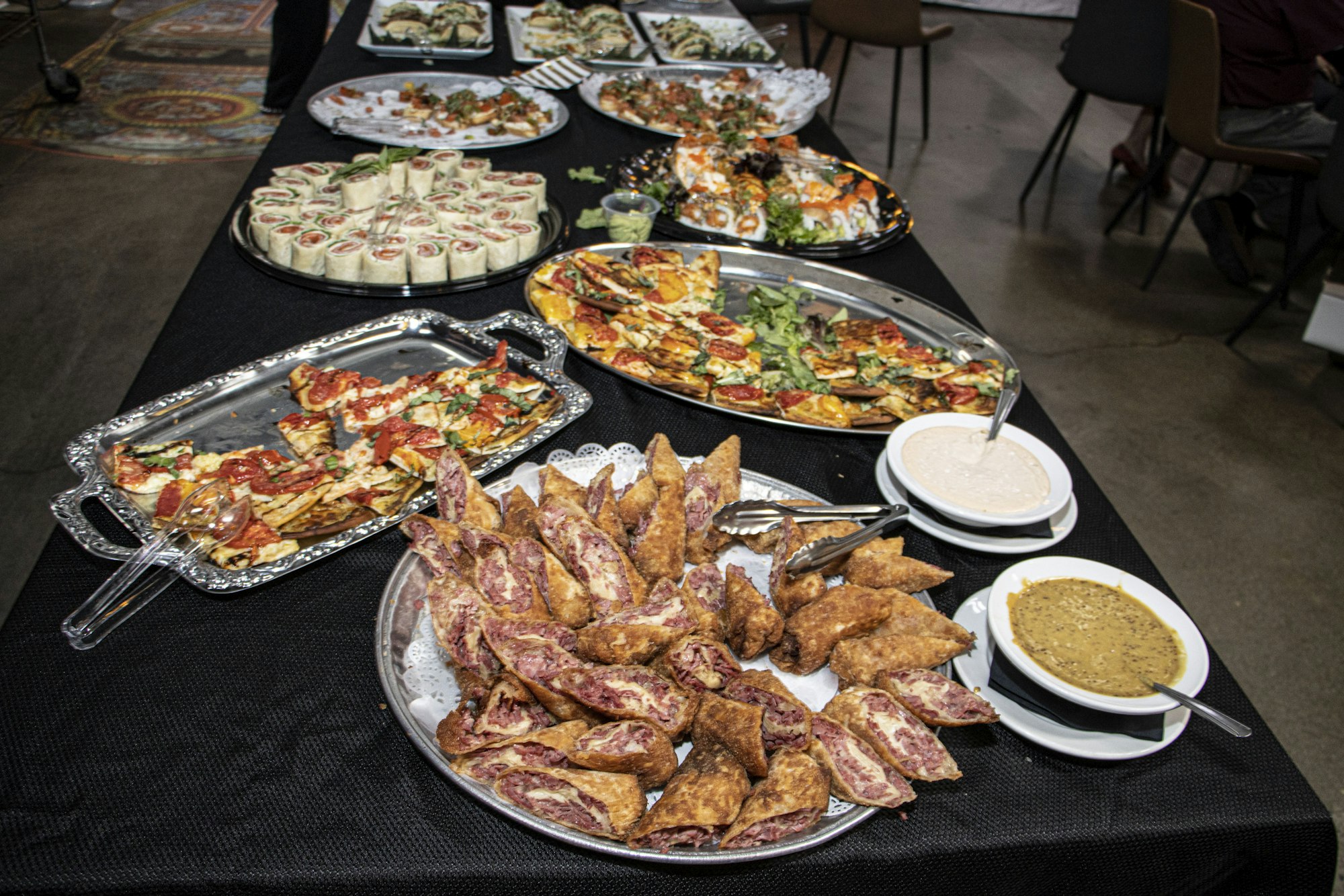 A buffet table with wraps, pizzas, stuffed pastries, dipping sauces, and assorted appetizers.