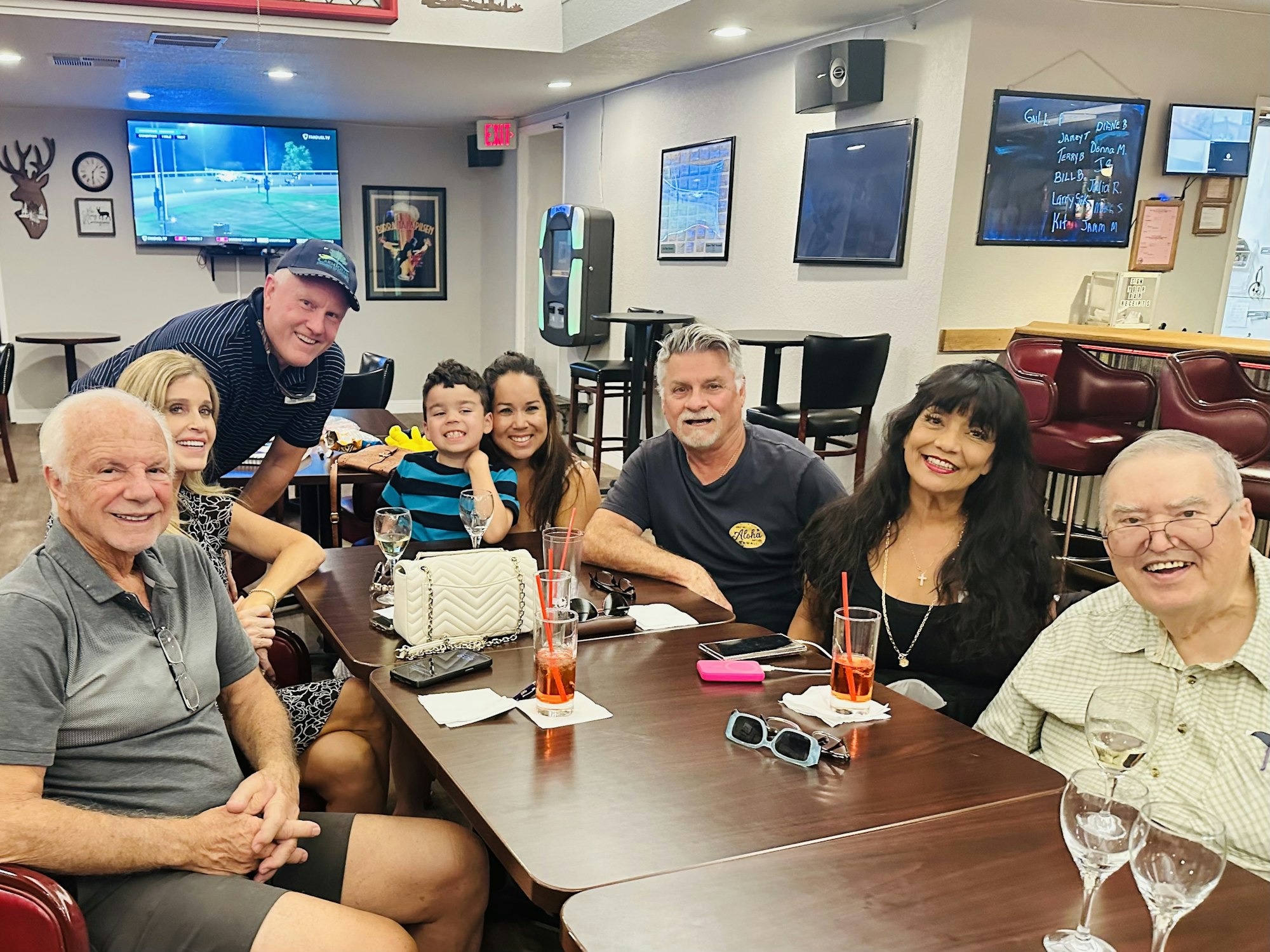 A group of people sitting around a table in a bar or restaurant, with drinks and smiling at the camera.