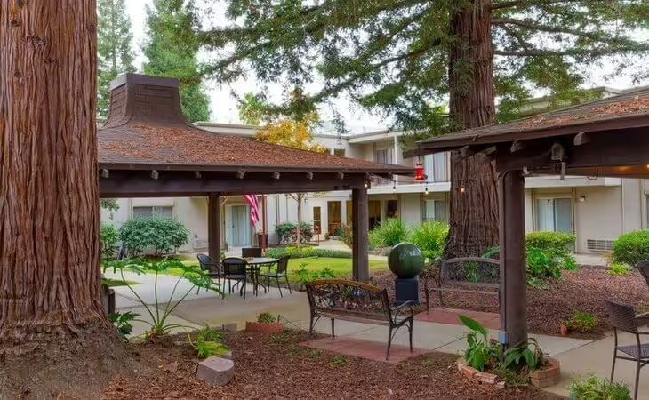 Outdoor seating area with tables and benches, surrounded by trees and buildings, with an American flag visible in the background.