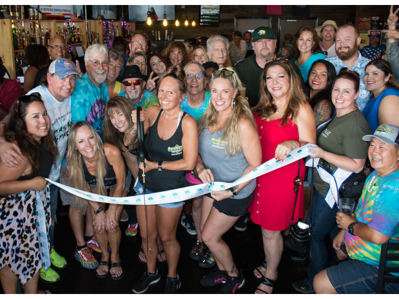 A large group of people, smiling, gathered indoors for a ribbon-cutting event.