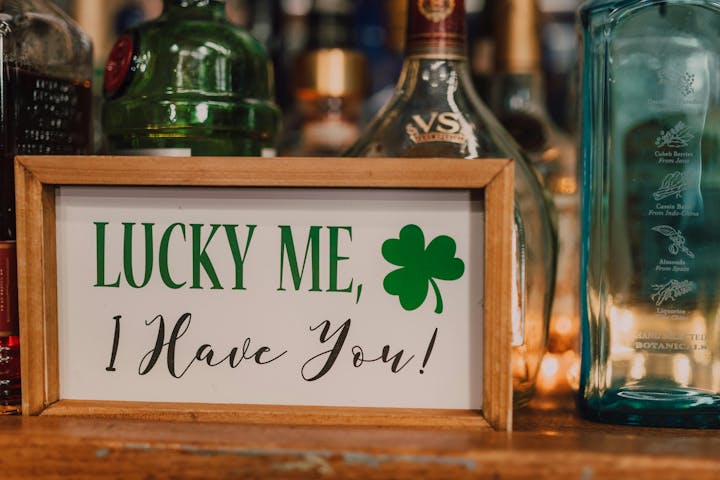 A framed sign reads “Lucky Me, I Have You!” with a green shamrock, surrounded by various bottles.