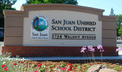 Sign for San Juan Unified School District at 3738 Walnut Avenue, with flowers in the foreground.