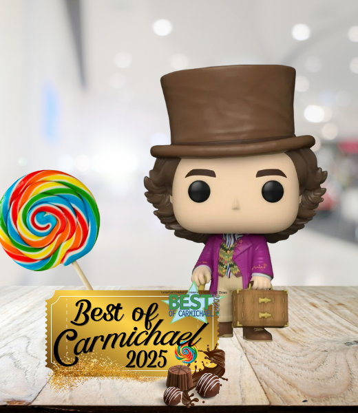 A figure with a top hat and suitcase stands beside a large colorful lollipop and a "Best of Carmichael 2025" sign on a table.