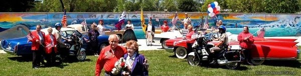 Parade of decorated, patriotic mini cars with senior drivers in an outdoor setting.