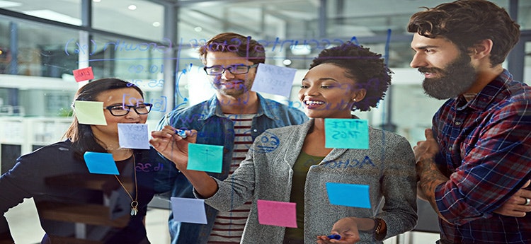 A group of four people collaborating at a glass board with sticky notes and writing on it.
