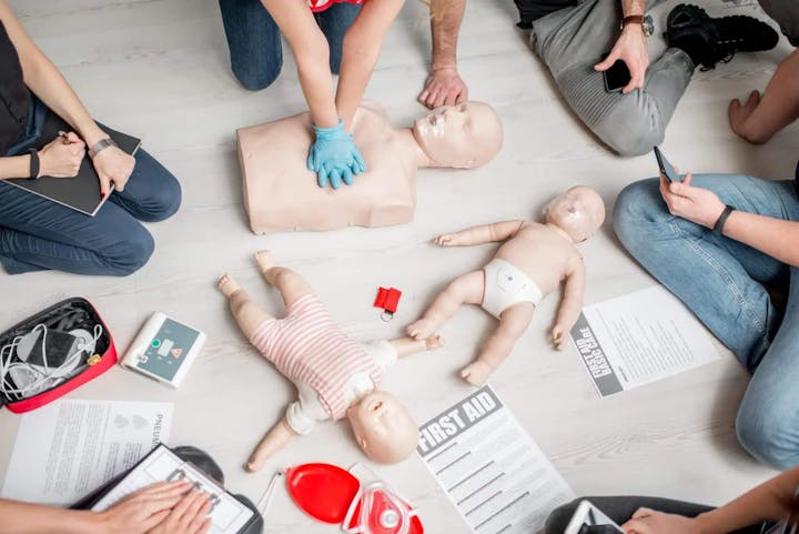 A CPR training session with people practicing on adult and infant mannequins, surrounded by first aid materials.