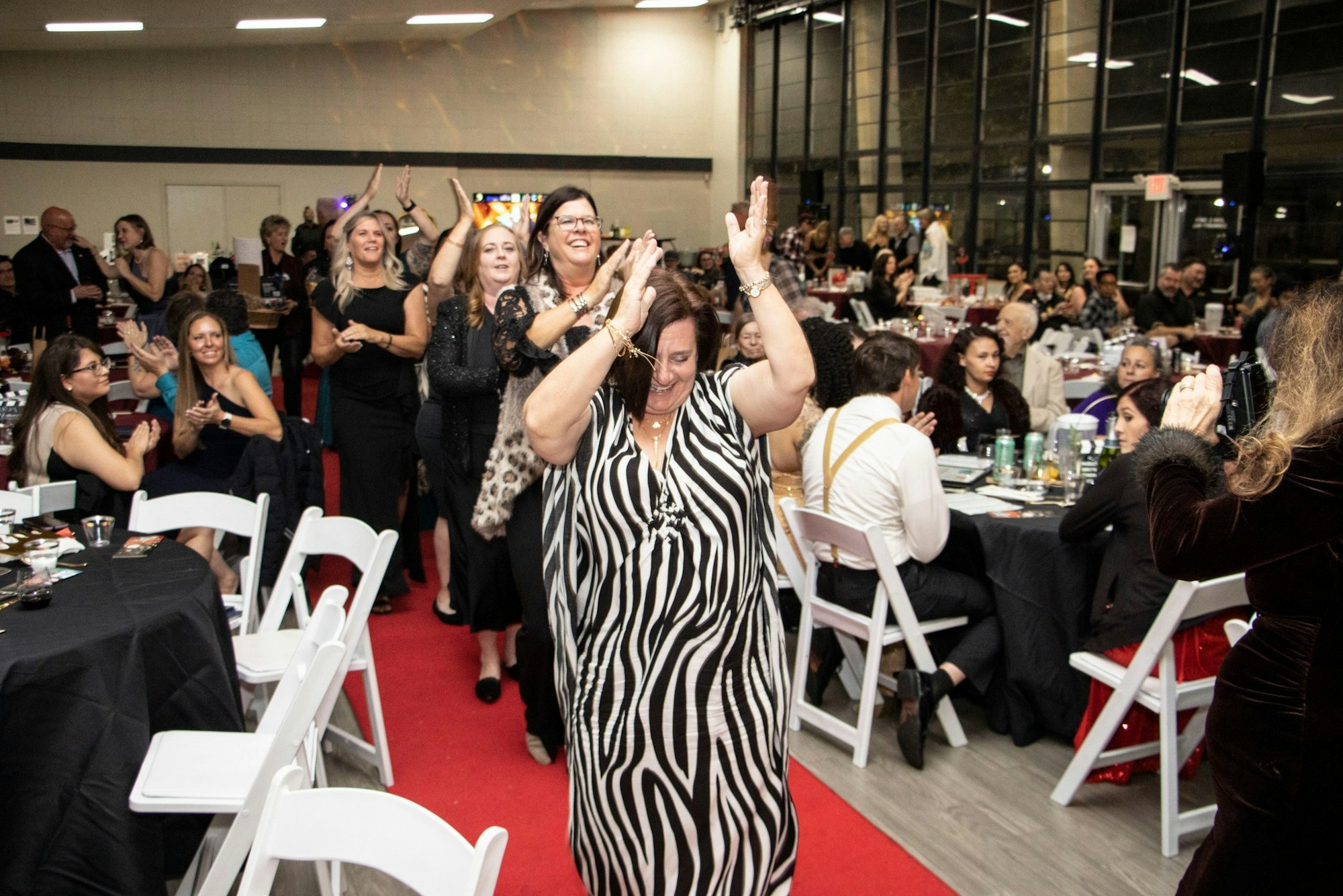 People enjoying a lively event, clapping and dancing in a decorated indoor venue with seated guests.