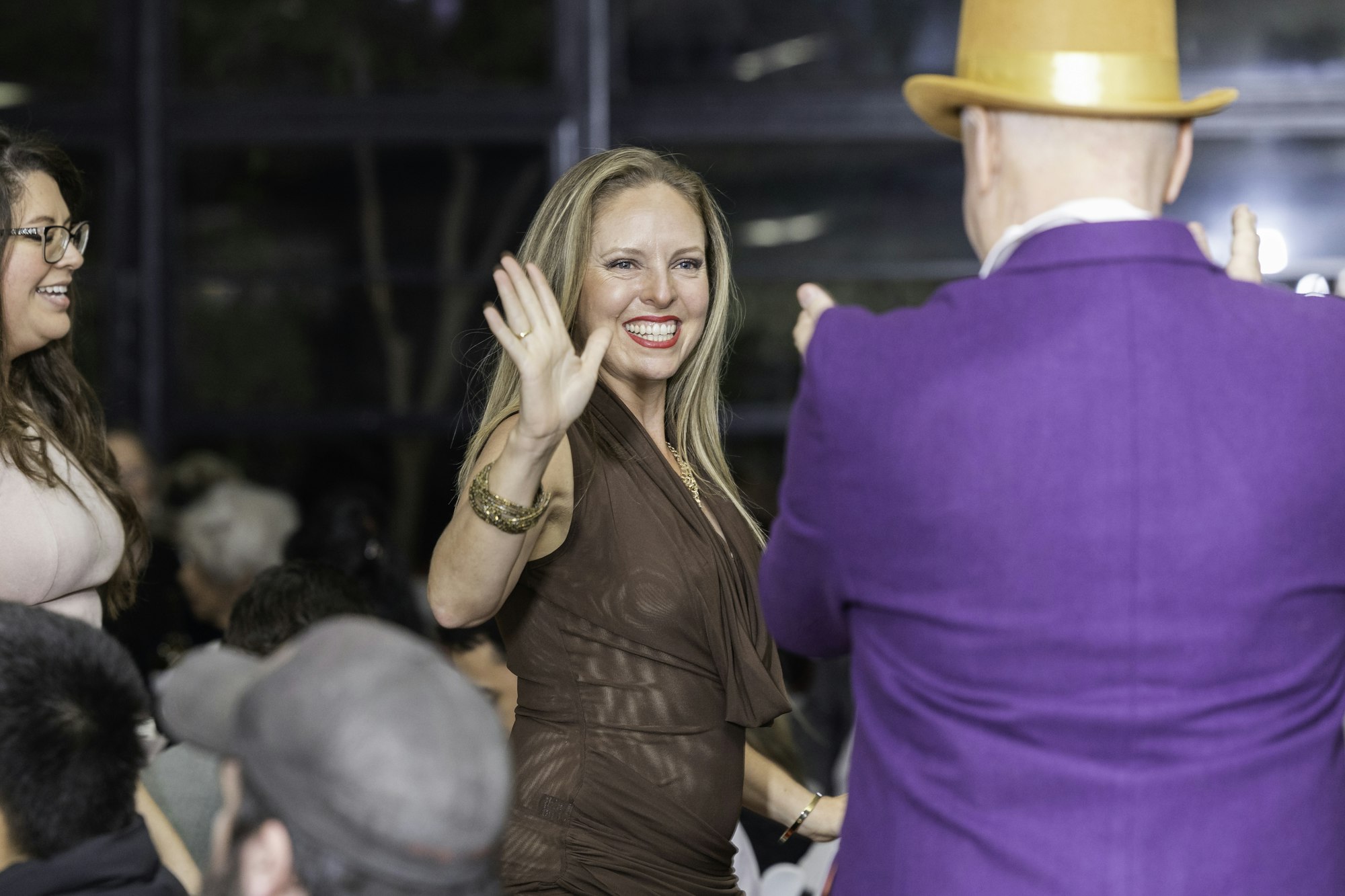 A woman in brown and a man in a purple suit with an orange hat are high-fiving at an event.