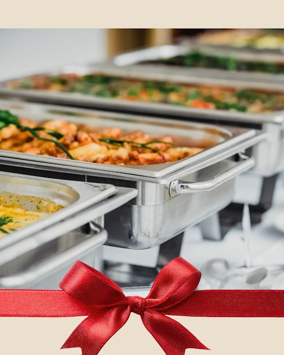 The image features a buffet setup with various dishes in stainless steel trays, adorned with a red ribbon graphic at the bottom.