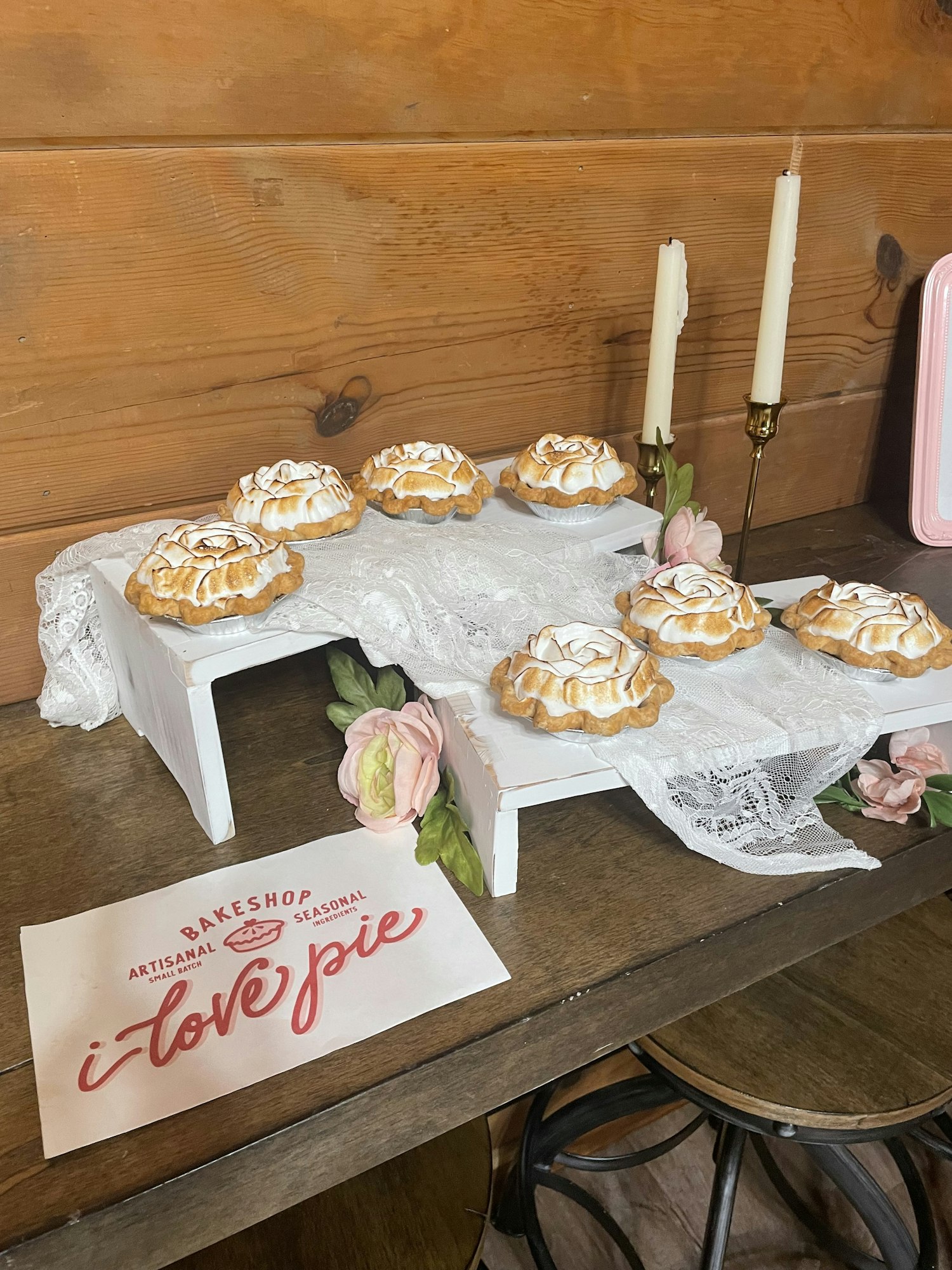 Mini pies with meringue tops on a wooden table, alongside flowers and a sign saying "i love pie".