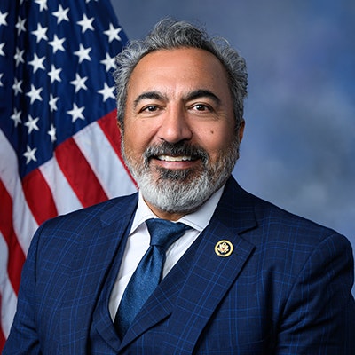 A man in a suit with a U.S. flag in the background.