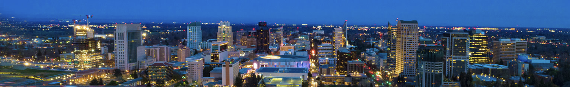 City skyline at dusk with illuminated buildings and a deep blue sky in the background.